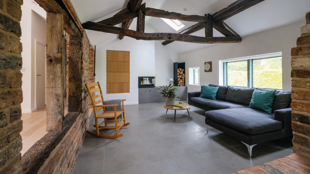 This is an example of a medium sized farmhouse open plan living room in West Midlands with white walls, concrete flooring, a corner fireplace, a plastered fireplace surround, grey floors, a vaulted ceiling and brick walls.