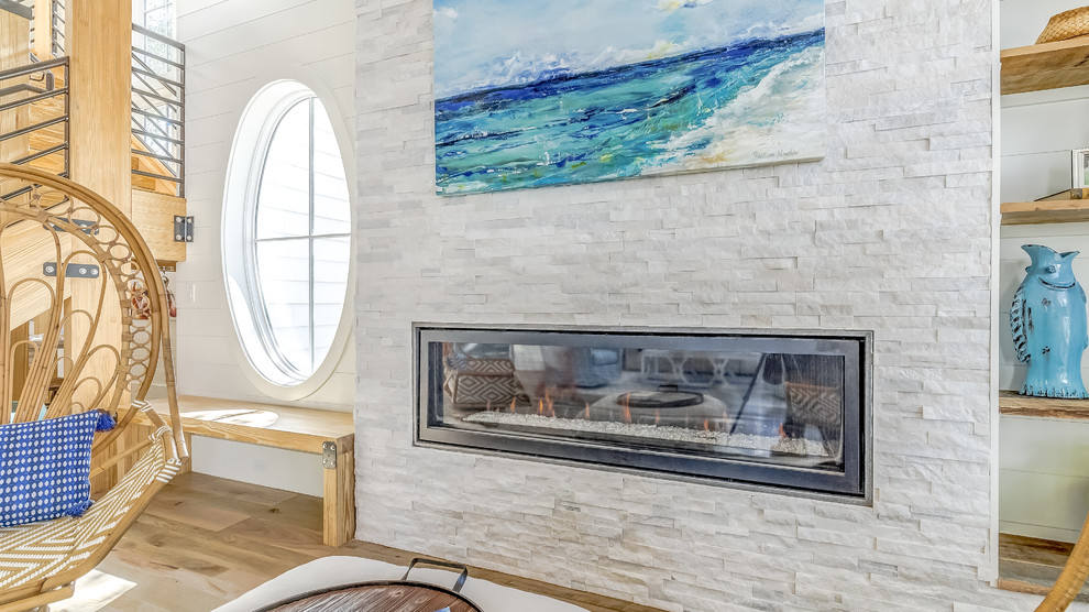 Immagine di un ampio soggiorno stile marino aperto con pareti bianche, pavimento in legno massello medio, cornice del camino in pietra, nessuna TV e pavimento marrone