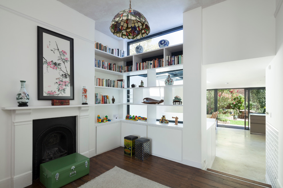 Пример оригинального дизайна: открытая гостиная комната в стиле фьюжн с с книжными шкафами и полками, белыми стенами, темным паркетным полом и стандартным камином