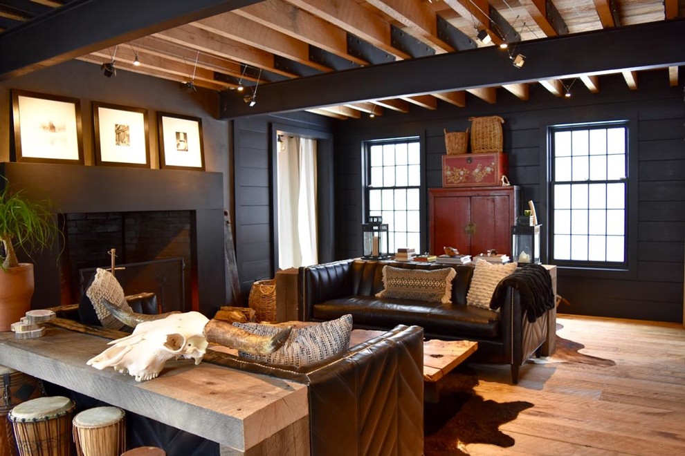 Idée de décoration pour un grand salon urbain ouvert avec un mur noir, un sol en bois brun, une cheminée standard et un manteau de cheminée en béton.