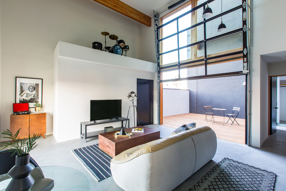 Ejemplo de salón abierto actual con paredes blancas, suelo de cemento, televisor independiente y suelo gris