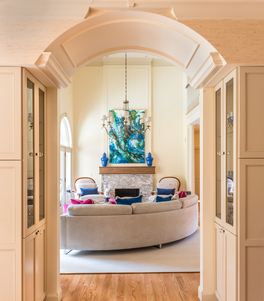 Diseño de salón abierto clásico renovado grande con paredes beige, suelo de madera clara y marco de chimenea de piedra