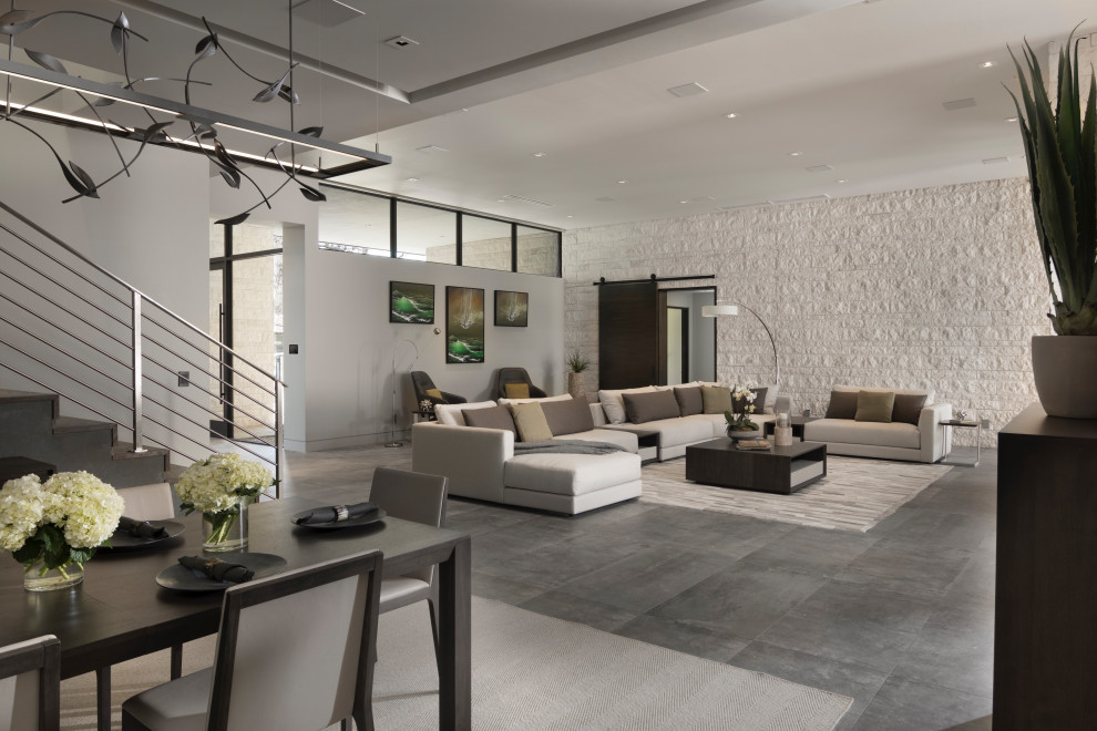 Design ideas for an expansive contemporary open plan living room in Las Vegas with multi-coloured walls, porcelain flooring, a two-sided fireplace, a brick fireplace surround, a wall mounted tv and grey floors.