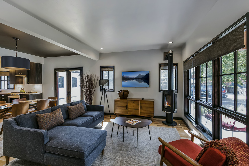 Стильный дизайн: гостиная комната в современном стиле с белыми стенами, деревянным полом, печью-буржуйкой и телевизором на стене - последний тренд