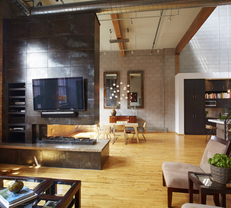 Foto de salón tipo loft industrial de tamaño medio con paredes beige, suelo de madera clara, chimenea de doble cara, marco de chimenea de metal, televisor colgado en la pared y suelo marrón