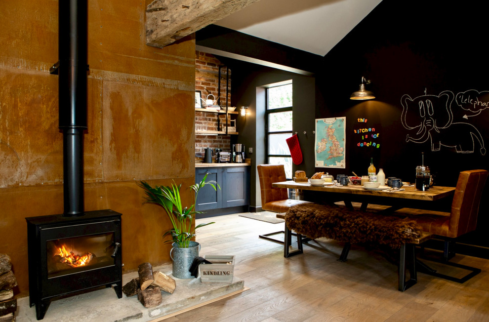 Living room - mid-sized eclectic open concept medium tone wood floor, brown floor, vaulted ceiling and brick wall living room idea in Other with black walls, a wood stove, a metal fireplace and a wall-mounted tv
