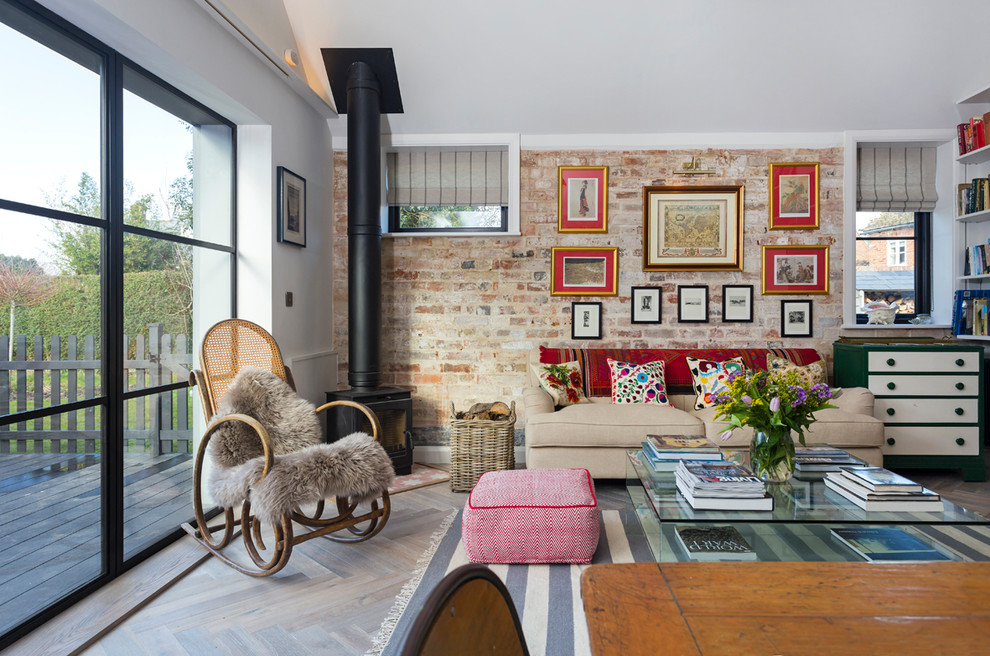 Idées déco pour un salon éclectique ouvert avec un mur rouge, parquet clair, un poêle à bois, un manteau de cheminée en métal et un sol beige.