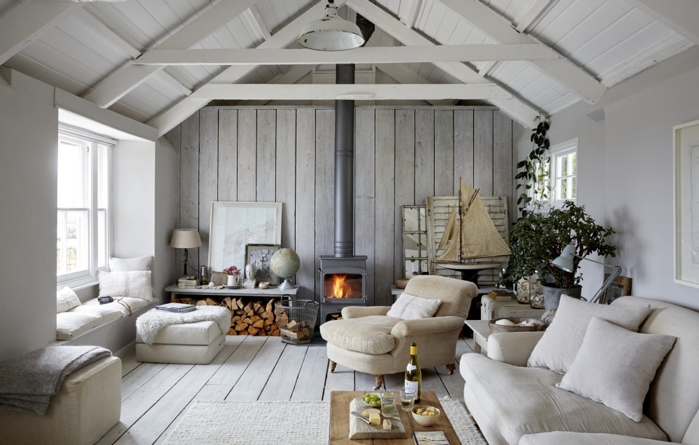 Großes Landhaus Wohnzimmer mit weißer Wandfarbe, gebeiztem Holzboden, Kaminofen, Kaminumrandung aus Holz und weißem Boden in Cornwall