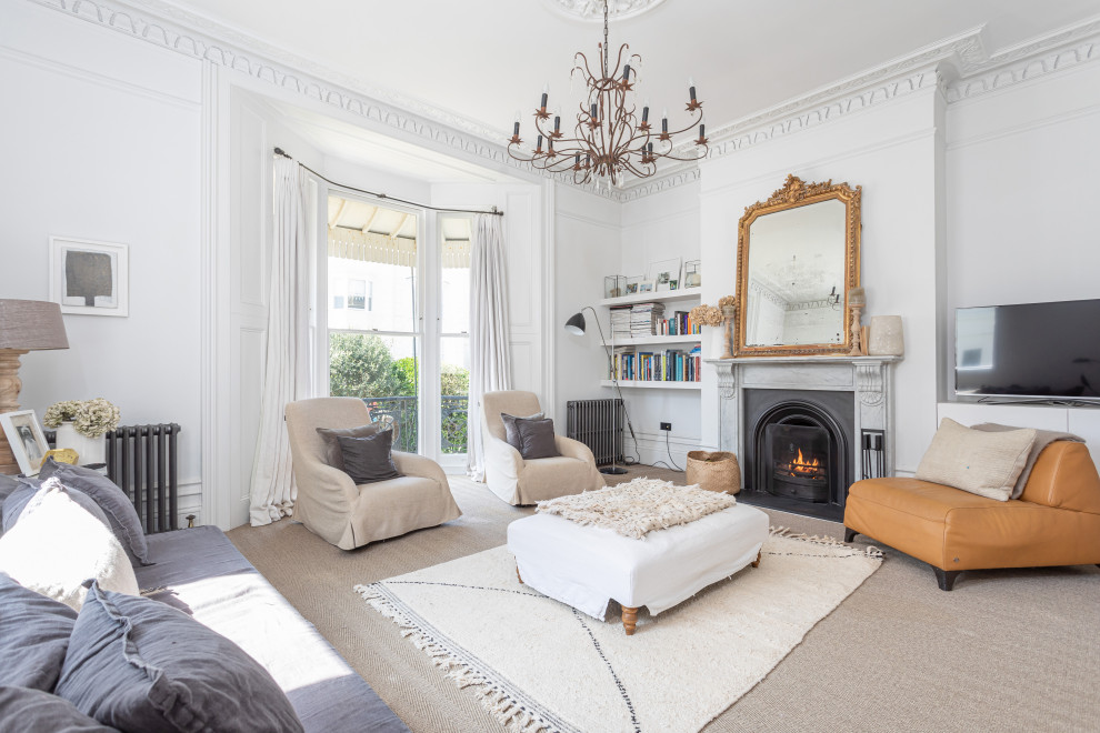 На фото: гостиная комната в стиле неоклассика (современная классика) с белыми стенами, ковровым покрытием, стандартным камином, отдельно стоящим телевизором, серым полом и эркером