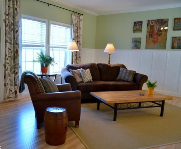 На фото: открытая гостиная комната среднего размера в стиле кантри с зелеными стенами, полом из ламината, стандартным камином, фасадом камина из дерева и коричневым полом с