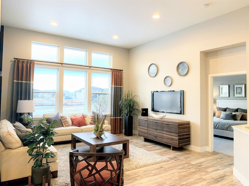 This is an example of a large contemporary open plan living room in Denver with a wall mounted tv, beige walls and light hardwood flooring.