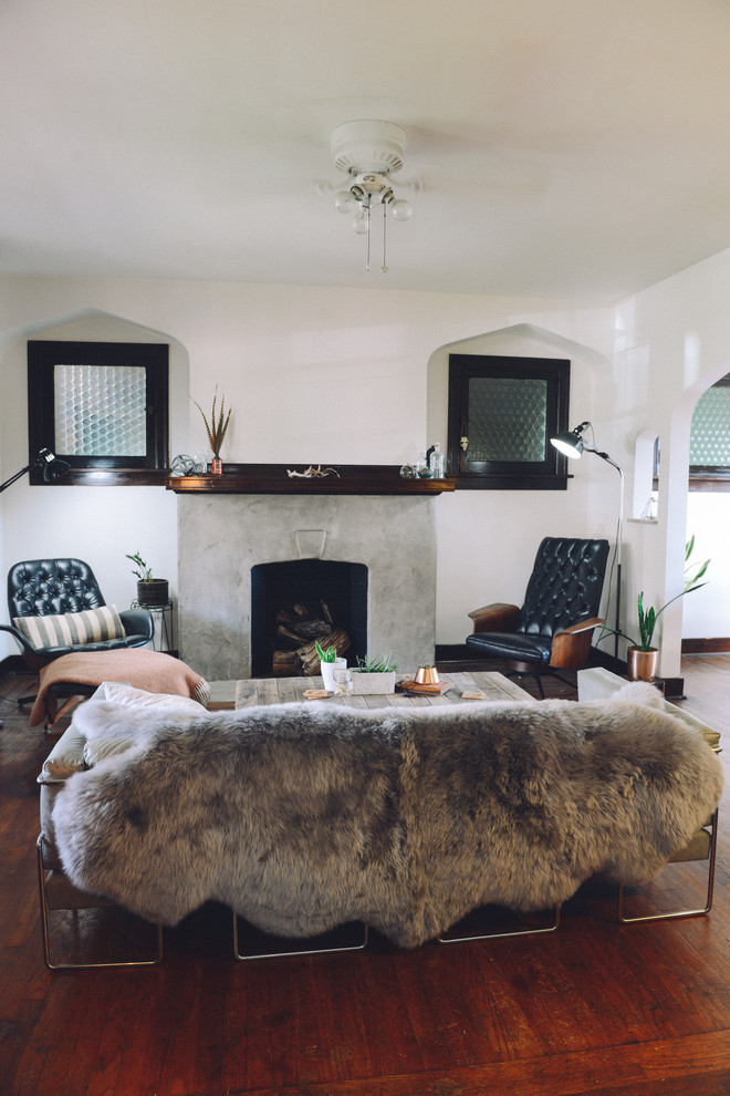 Cette photo montre un salon éclectique de taille moyenne et fermé avec un mur blanc, un sol en bois brun, une cheminée standard, un manteau de cheminée en béton et aucun téléviseur.
