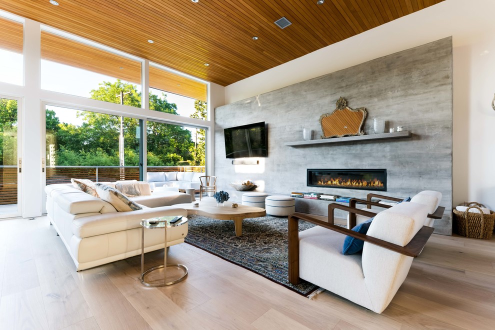 Imagen de salón abierto contemporáneo con suelo de madera clara, marco de chimenea de hormigón, televisor colgado en la pared y chimenea lineal