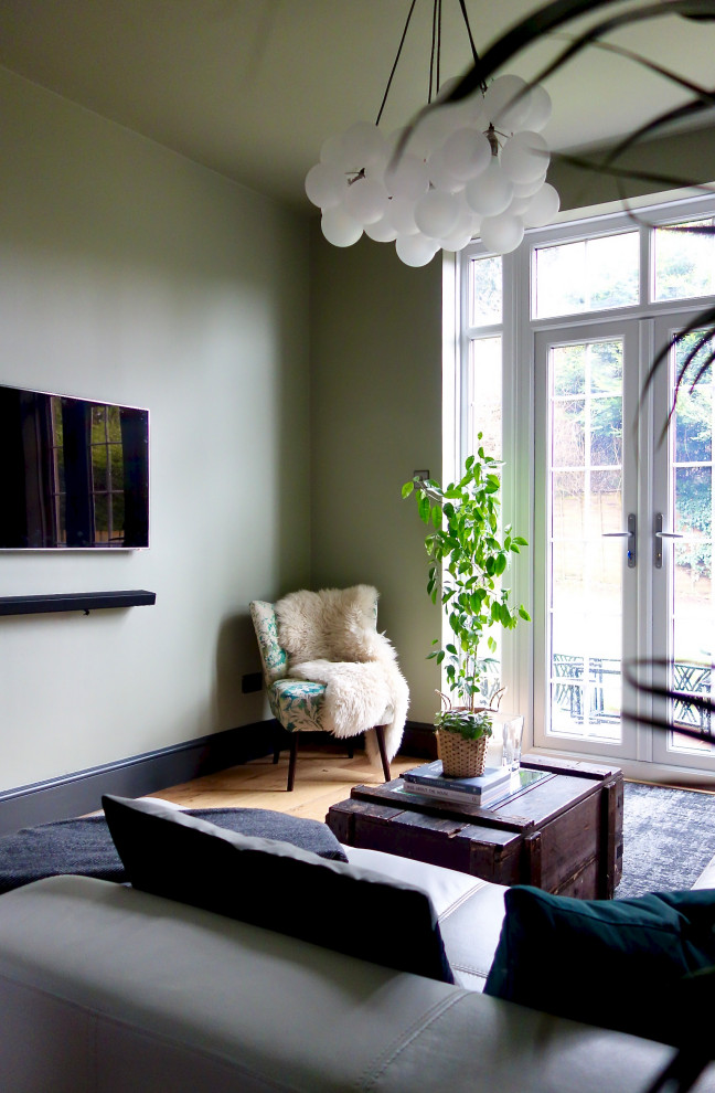 Immagine di un soggiorno bohémian di medie dimensioni con angolo bar, pareti verdi, pavimento in legno massello medio e TV a parete