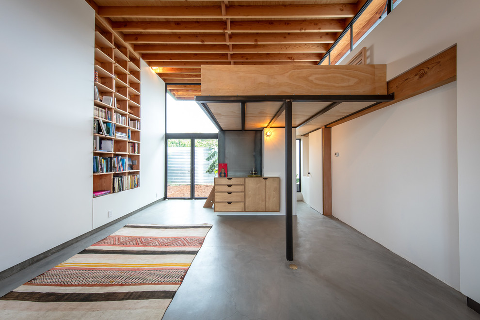 Immagine di un piccolo soggiorno design stile loft con libreria, pareti bianche e pavimento in cemento