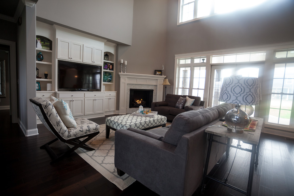 Exemple d'un salon chic ouvert avec un mur gris, parquet foncé, une cheminée d'angle, un manteau de cheminée en carrelage et un téléviseur encastré.