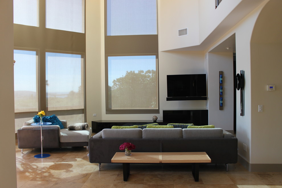 Пример оригинального дизайна: большая открытая гостиная комната в современном стиле с белыми стенами, полом из травертина, стандартным камином, фасадом камина из камня и телевизором на стене