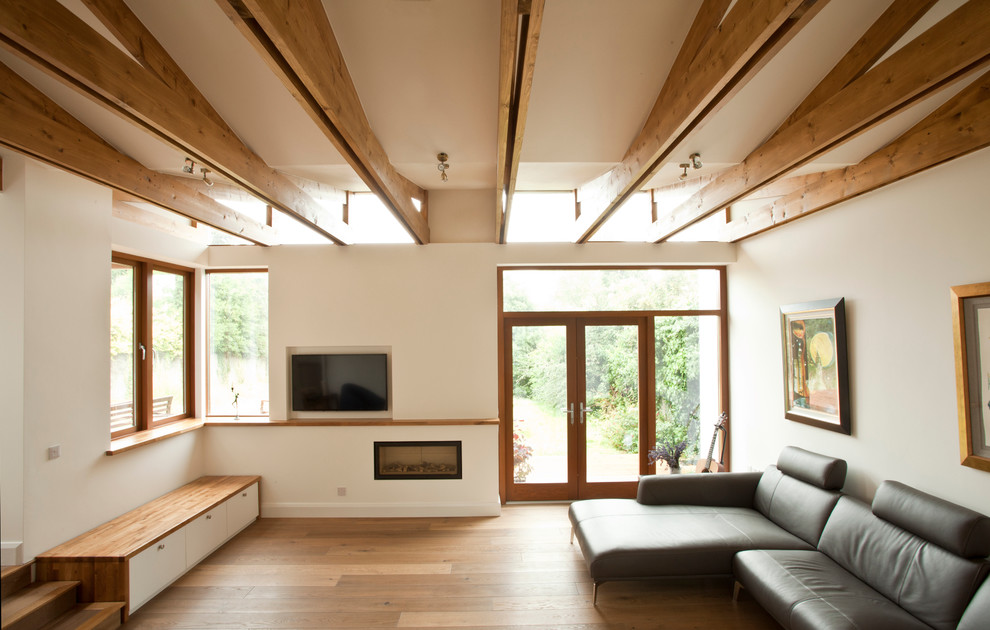 Стильный дизайн: большая открытая гостиная комната в современном стиле с белыми стенами, светлым паркетным полом и телевизором на стене - последний тренд