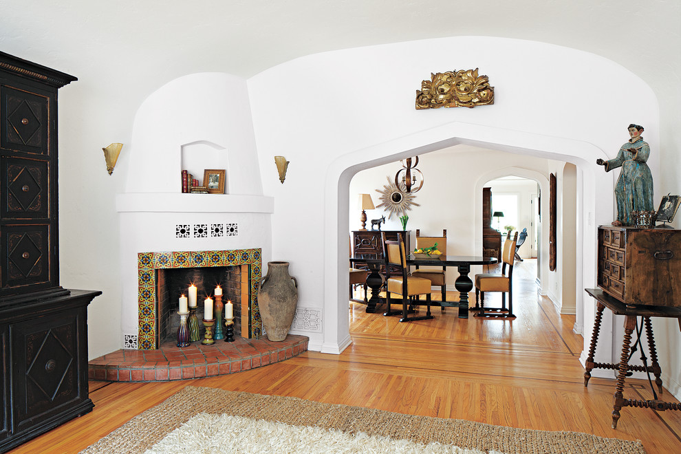 Inspiration pour un salon méditerranéen avec un mur blanc, un sol en bois brun, une cheminée d'angle et un manteau de cheminée en carrelage.