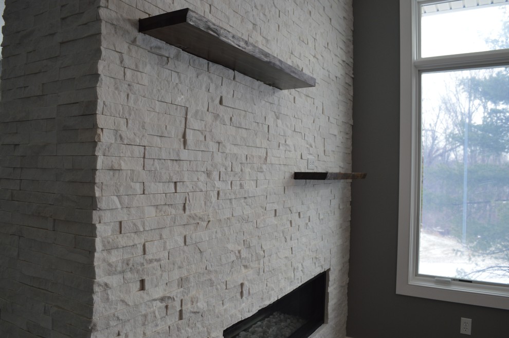 Cette image montre un grand salon craftsman ouvert avec un mur gris, parquet foncé, une cheminée double-face, un manteau de cheminée en pierre, un téléviseur fixé au mur et un sol marron.