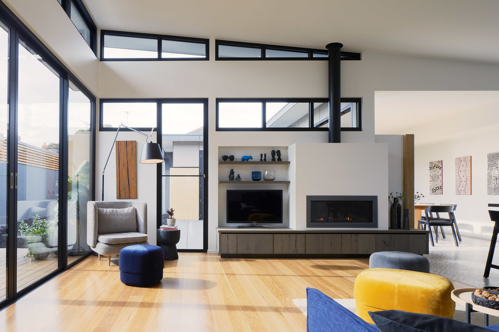Diseño de salón abierto actual con paredes blancas, suelo de madera en tonos medios, chimenea lineal, televisor independiente y suelo marrón