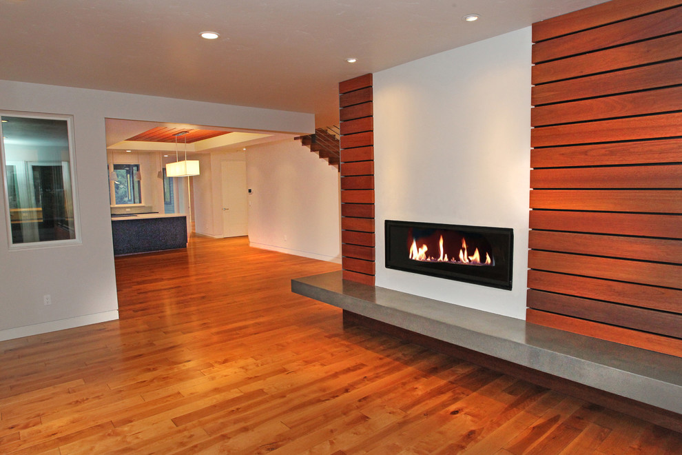 Aménagement d'un salon contemporain de taille moyenne et ouvert avec un mur blanc, un sol en bois brun, un manteau de cheminée en béton et un téléviseur dissimulé.
