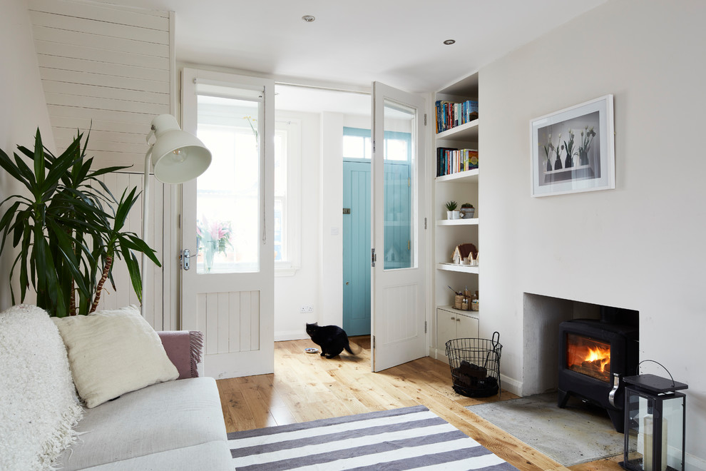 Aménagement d'un petit salon scandinave ouvert avec un mur blanc, parquet clair, un poêle à bois, un manteau de cheminée en plâtre, aucun téléviseur, un sol marron et éclairage.