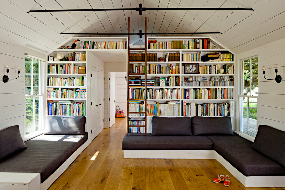 Aménagement d'un salon campagne avec une bibliothèque ou un coin lecture, un mur blanc et un sol en bois brun.