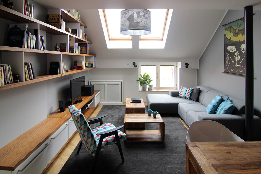 Modern inredning av ett litet separat vardagsrum, med grå väggar, ljust trägolv och en fristående TV