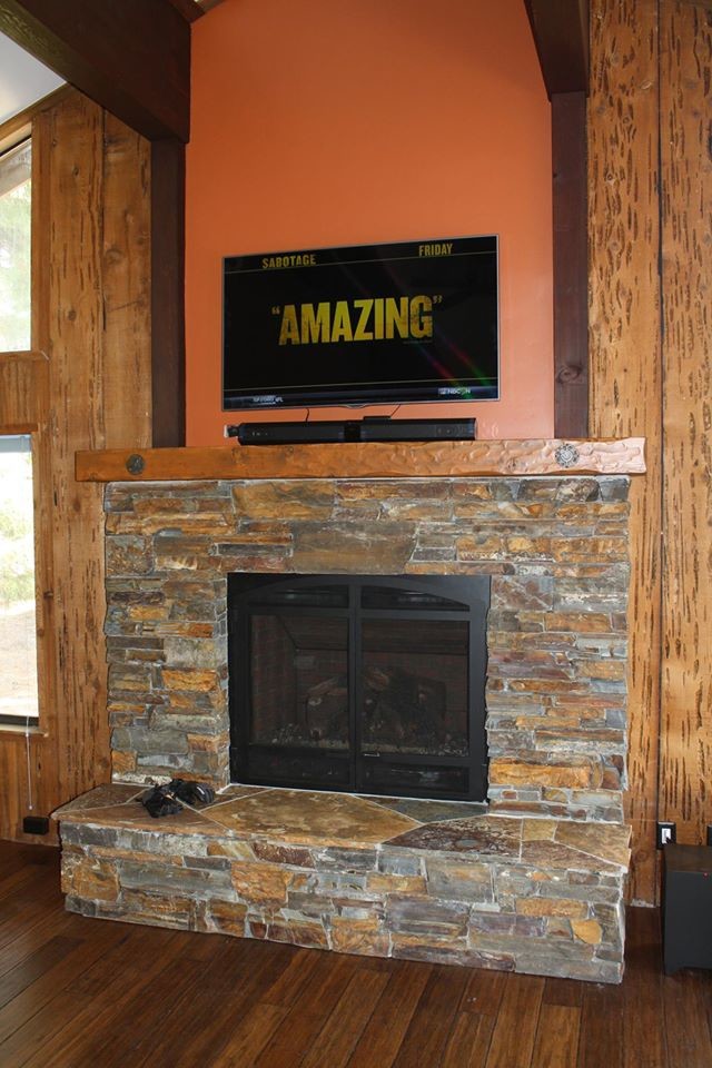 サクラメントにある高級な広いラスティックスタイルのおしゃれなリビング (オレンジの壁、無垢フローリング、標準型暖炉、石材の暖炉まわり、壁掛け型テレビ) の写真