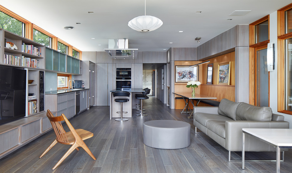 Imagen de salón abierto contemporáneo con paredes grises, suelo de madera en tonos medios, pared multimedia y suelo gris