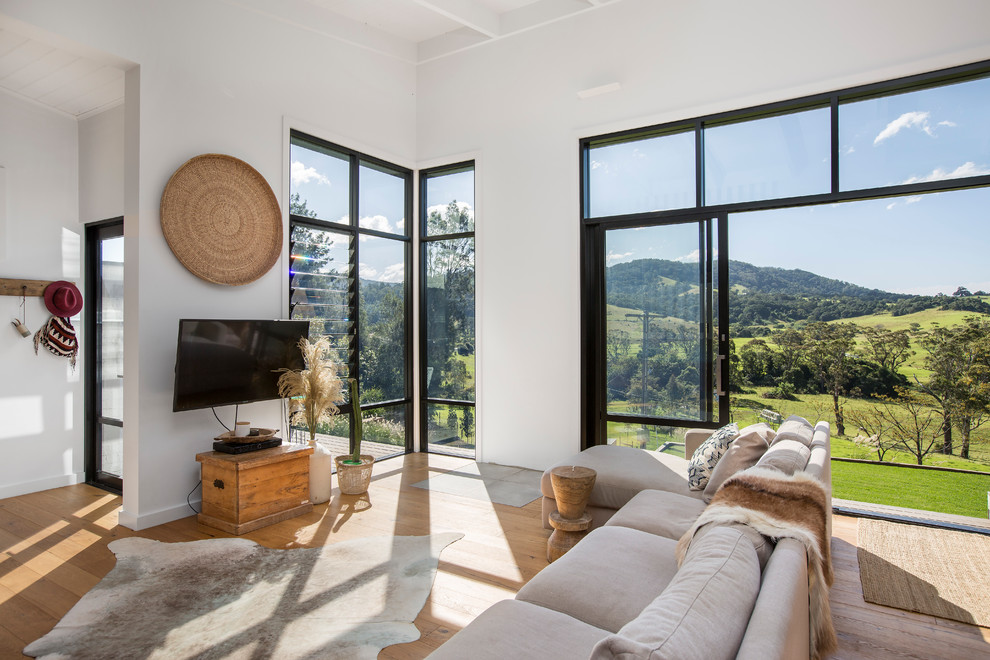 Offenes Maritimes Wohnzimmer ohne Kamin mit weißer Wandfarbe, hellem Holzboden, TV-Wand und braunem Boden in Wollongong