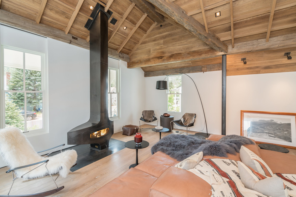 Diseño de salón abierto de estilo de casa de campo grande con paredes blancas, suelo de madera clara, estufa de leña, marco de chimenea de metal y suelo gris