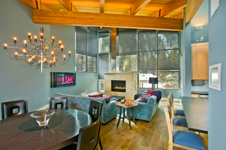 Exemple d'un salon tendance de taille moyenne et ouvert avec un mur bleu, un sol en bois brun, une cheminée standard, un manteau de cheminée en pierre et un téléviseur encastré.