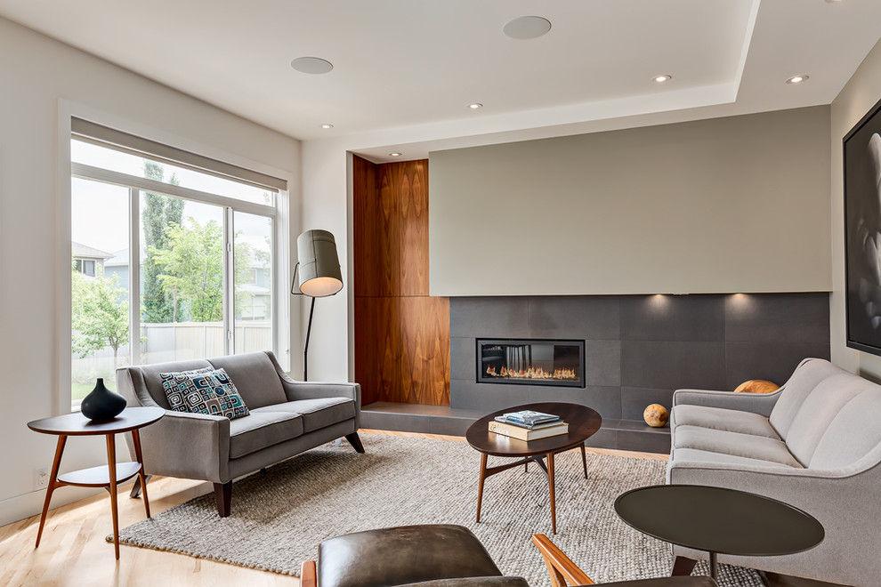 Contemporary living room in Calgary with grey walls, light hardwood flooring, a ribbon fireplace and a tiled fireplace surround.