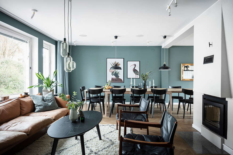 Стильный дизайн: большая открытая гостиная комната в скандинавском стиле с синими стенами, темным паркетным полом, стандартным камином, фасадом камина из штукатурки, телевизором на стене и коричневым полом - последний тренд