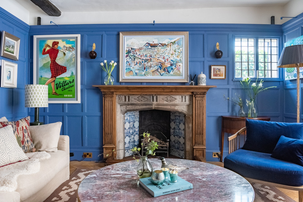 This is an example of a large bohemian enclosed living room in London with a reading nook, blue walls, light hardwood flooring, a standard fireplace, a stone fireplace surround, a concealed tv, beige floors, exposed beams and wood walls.