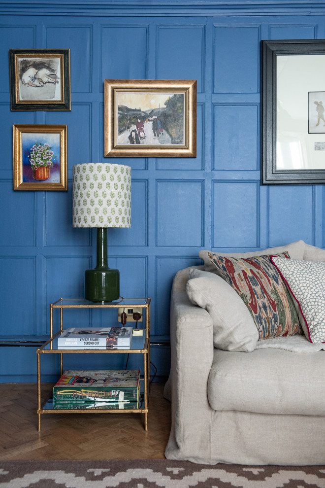 Foto på ett stort eklektiskt separat vardagsrum, med ett bibliotek, blå väggar, ljust trägolv, en standard öppen spis, en spiselkrans i sten, en dold TV och beiget golv