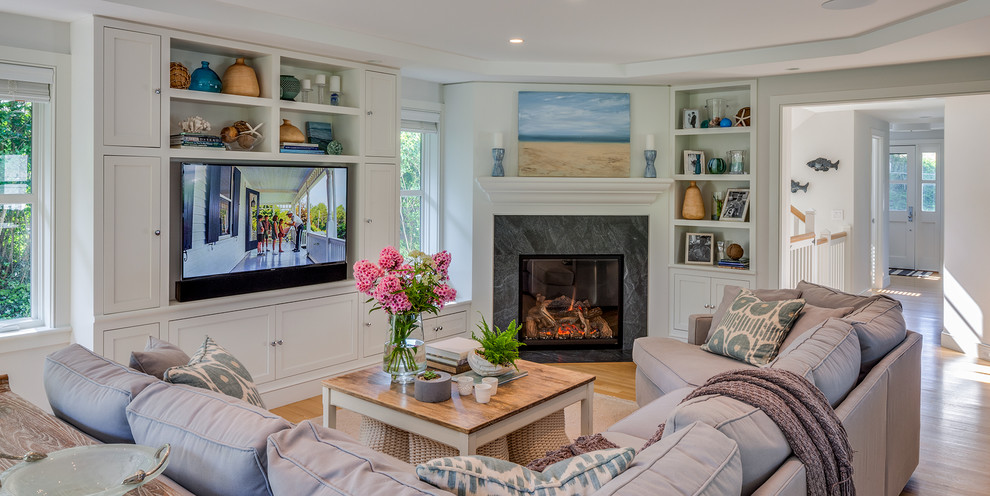 Beach style living room in Boston with grey walls, light hardwood flooring, a corner fireplace, a tiled fireplace surround, a built-in media unit and beige floors.