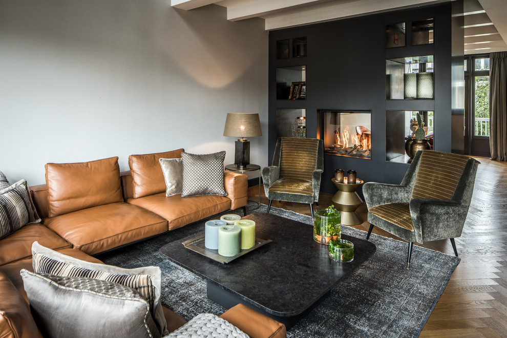 This is an example of a contemporary grey and brown enclosed living room in Amsterdam with grey walls, medium hardwood flooring and a two-sided fireplace.