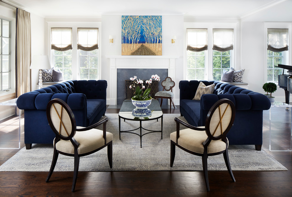 Пример оригинального дизайна: парадная гостиная комната в классическом стиле с темным паркетным полом, стандартным камином, белыми стенами и синим диваном без телевизора