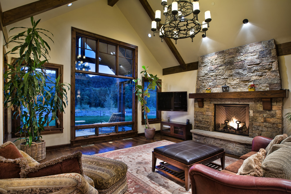 Mittelgroßes, Offenes Klassisches Wohnzimmer mit beiger Wandfarbe, dunklem Holzboden, Kaminumrandung aus Stein, Kamin, TV-Wand und braunem Boden in Denver