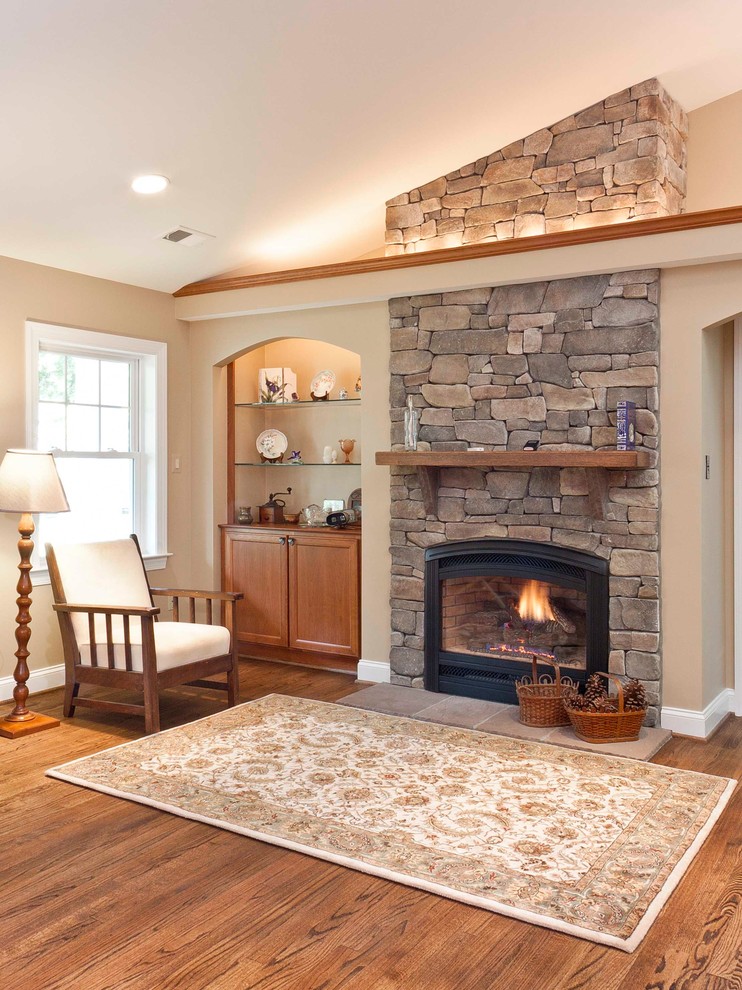 Cette photo montre un salon chic avec un mur beige, une cheminée standard, un manteau de cheminée en pierre et canapé noir.