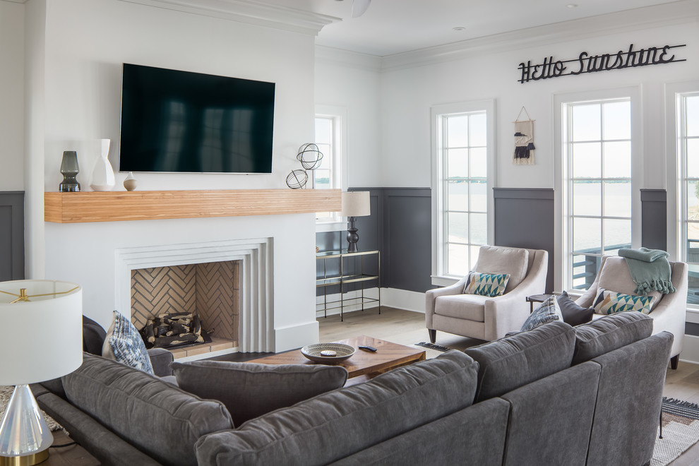 This is an example of a large coastal living room in Other with white walls, medium hardwood flooring, a standard fireplace, a plastered fireplace surround, a wall mounted tv and brown floors.