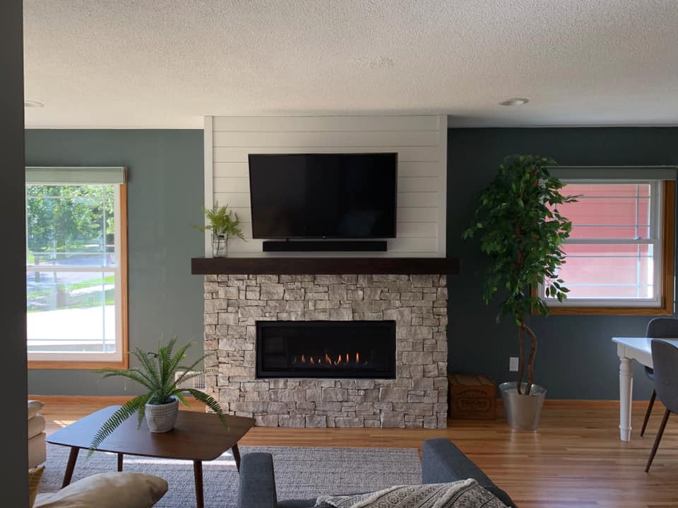 Idée de décoration pour un salon tradition ouvert avec une salle de réception, un mur vert, une cheminée standard, un manteau de cheminée en pierre, un téléviseur fixé au mur et un sol marron.