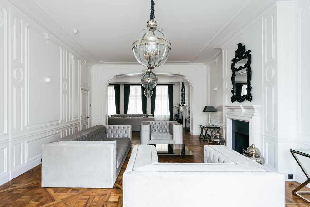 Пример оригинального дизайна: огромная парадная, открытая гостиная комната в стиле неоклассика (современная классика) с белыми стенами, паркетным полом среднего тона и стандартным камином без телевизора