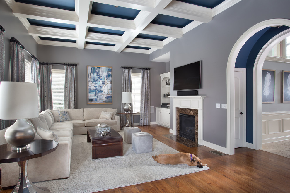 Inspiration pour un grand salon traditionnel avec un mur gris, un sol en bois brun, une cheminée standard, un manteau de cheminée en pierre, un téléviseur fixé au mur et un sol marron.