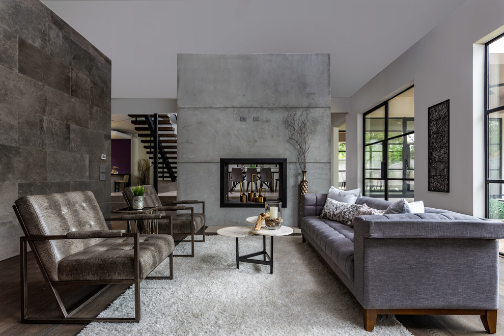 Стильный дизайн: открытая гостиная комната в современном стиле с серыми стенами, темным паркетным полом, двусторонним камином, фасадом камина из бетона и коричневым полом - последний тренд