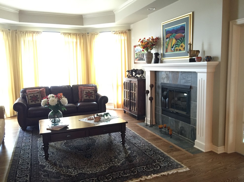 Cette image montre un grand salon traditionnel avec un mur beige, un sol en bois brun, un téléviseur indépendant, une cheminée standard, un manteau de cheminée en carrelage et un sol marron.