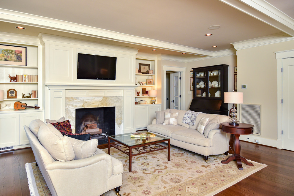 Offenes Klassisches Wohnzimmer mit beiger Wandfarbe, dunklem Holzboden, Kamin, Kaminumrandung aus Stein, TV-Wand und braunem Boden in Sonstige